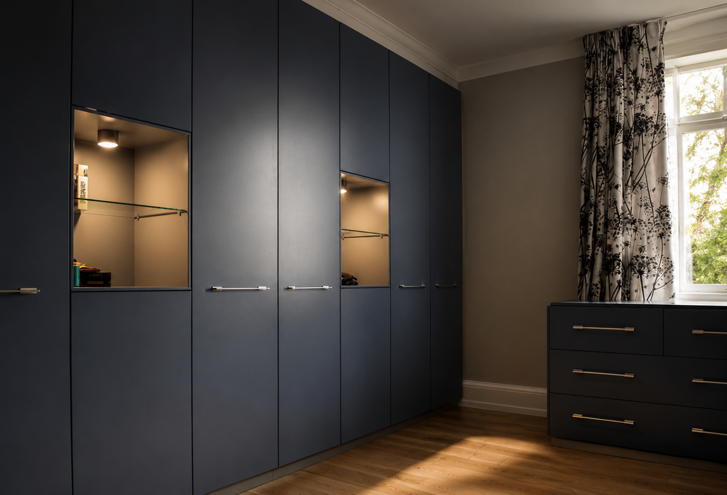 Custom midnight-blue wardrobe wall with integrated lit display niches and matching dresser