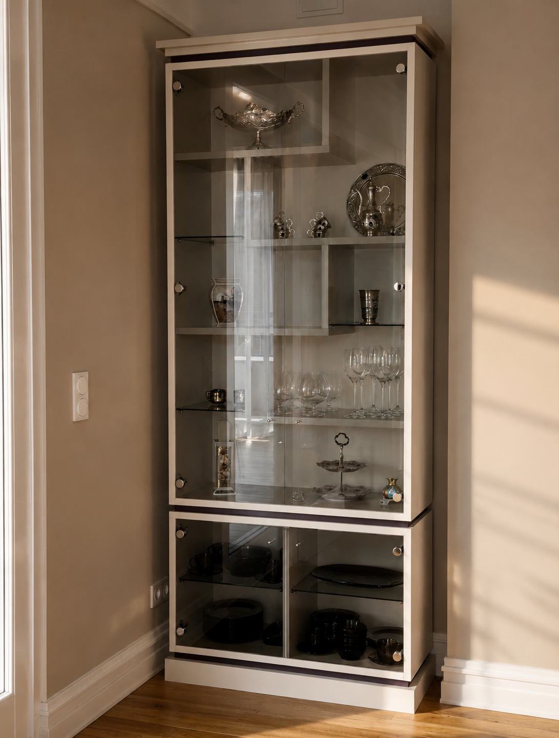 Bespoke glass vitrine with silver objects and stemware in a warm neutral interior